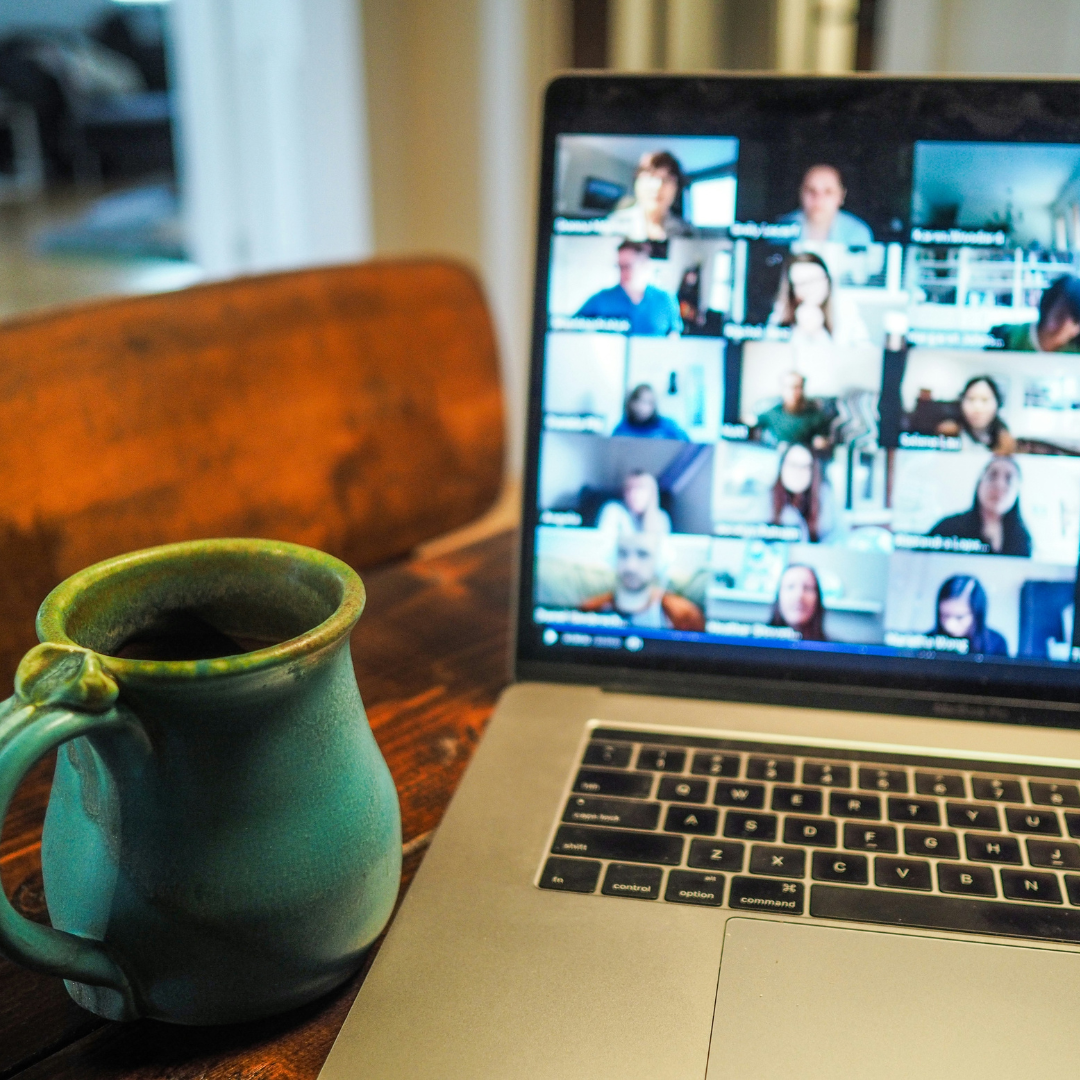 A laptop with a zoom call on the screen and a ceremic mug next to it on a table